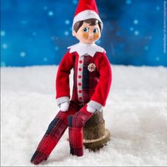 an elf sitting on top of a tree stump in the snow wearing a red and black outfit