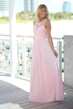 a woman in a long pink dress standing on a porch with her hands in her pockets