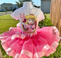 a pink tutu skirt and t - shirt with princess peaches on it sitting in the grass