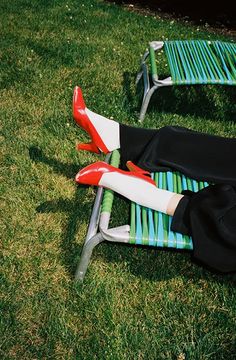 a woman laying on top of a green lawn next to two blue metal park benches