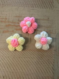 three crocheted flowers sitting on top of a wooden table