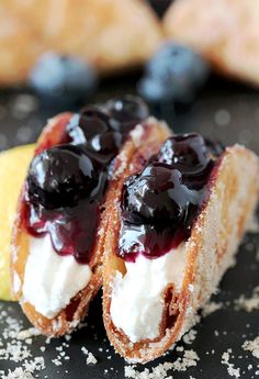 two pastries with blueberries and cream are on a black surface next to lemon wedges