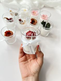 a hand holding a small glass container with flowers in it and several other cups behind it