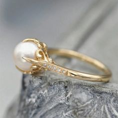 a pearl and diamond ring sitting on top of a rock