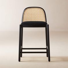 a black chair with a woven seat and backrest, on a white background in front of a beige wall