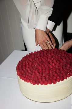 two people are cutting into a cake with raspberries on the top and bottom