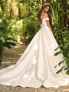 a woman in a white wedding dress standing on a stone path surrounded by greenery