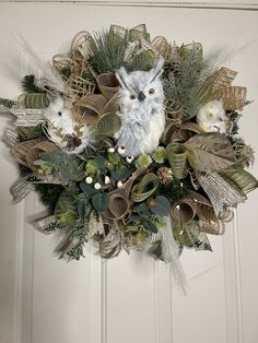 a wreath with an owl and two birds on it hanging from the front door, surrounded by greenery