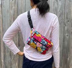 a woman wearing a pink shirt and blue pants with a colorful floral fanny bag on her back