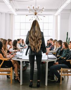 a woman standing in front of a group of people at a table with laptops