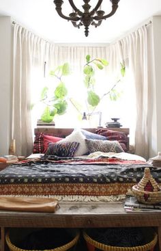 a bed sitting under a window next to a table with baskets on top of it