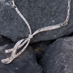 This bejeweld 14k white gold necklace features a ribbon motif accented with one (1) bezel set round brilliant cut diamond, thirty-nine (39) prong set round brilliant cut diamonds, and thirty-five (35) channel set baguette cut diamonds. The pendant measures 57mm by 52mm and is attached to a fancy link chain.  The overall length of the necklace is 17.5 inches. Silver Channel Set Diamond Necklace For Anniversary, Fine Jewelry Diamond Necklace With Channel Set, Elegant Formal Channel Set Necklaces, Elegant Channel Set Necklaces For Formal Occasions, Elegant Channel Set Necklace For Formal Occasions, Elegant White Gold Diamond Necklace Channel Set, Elegant Platinum Diamond Necklace With Baguette Diamonds, Elegant Cubic Zirconia Necklace Channel Set, Formal Round Diamond Necklace Channel Set