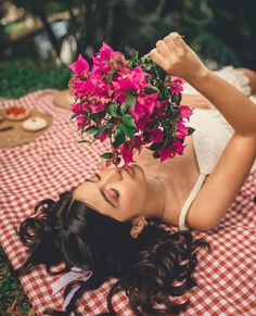 a beautiful woman laying on top of a red and white checkered blanket holding flowers