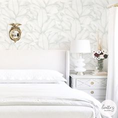 a white bed sitting in a bedroom next to a wall mounted mirror and two nightstands