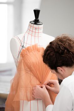 a woman is working on an orange piece of fabric in front of a mannequin