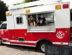 two people standing in the window of a red and white fire truck