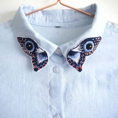 a blue shirt with an embroidered butterfly on the collar and two black eyes in the center