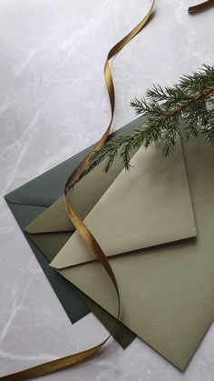 three envelopes with gold ribbon and evergreen branches on them, sitting next to each other