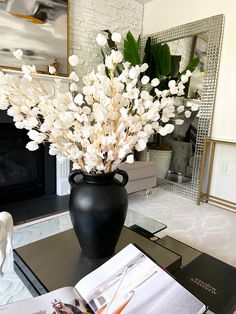 a black vase filled with white flowers sitting on top of a table next to a fireplace