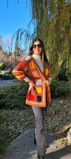 a woman standing in front of a tree wearing an orange and yellow knitted shawl