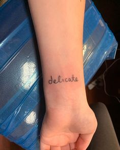 a woman's foot with the word delicate tattooed on her left side arm, in black ink