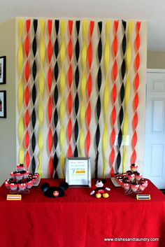 a red table topped with cake and cupcakes next to a wall covered in pictures