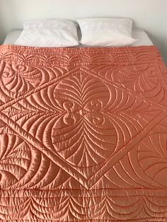 a bed with an orange quilt and white pillows