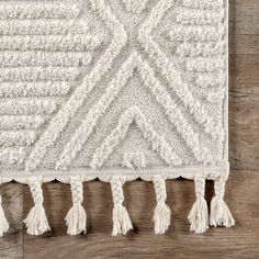 a white rug with tassels and fringe on top of a wooden floor next to a wall