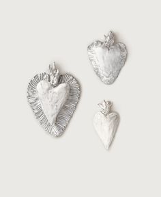 three silver heart shaped ornaments on a white background