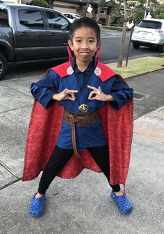 a young boy dressed up in a costume on the sidewalk with his hands folded out