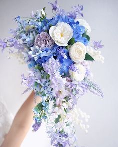 a woman holding a bouquet of flowers in her hand with white and blue flowers on it