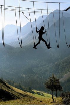 a person is suspended on ropes in the air above a grassy field and mountain range