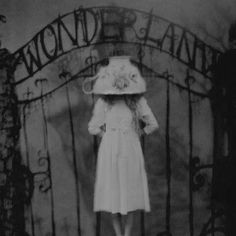 a woman standing in front of an iron gate wearing a white dress and large hat