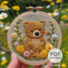 a hand holding up a small embroidered teddy bear with daisies in the foreground