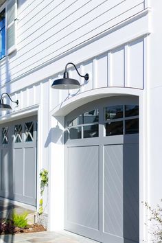 a white house with two garage doors and a lamp on the side of the building