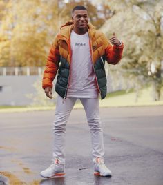 a man in an orange jacket and white t - shirt is standing on the street