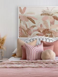 a bed with pink and green pillows on top of it next to a vase filled with flowers