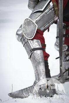 the legs and feet of a man in armor on snow covered ground, with one leg up