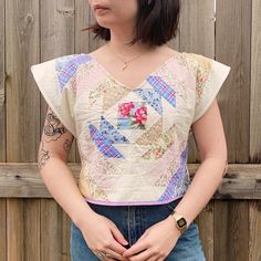 a woman standing in front of a wooden fence with her hands on her hips and looking off to the side