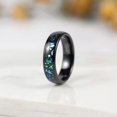 a black ring with blue and green inlays sitting on top of a white surface