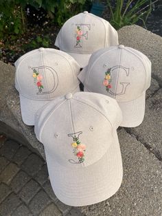 four baseball caps with flowers on them are sitting on the ground in front of some bushes