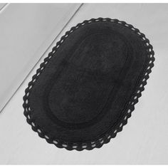 an oval black rug with scalloped edges on a white floor next to a door