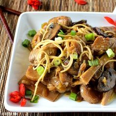 a white plate topped with noodles and meat next to chopsticks on a table