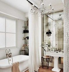 a white bath tub sitting under a chandelier next to a sink and toilet