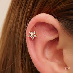 a woman's ear is adorned with three small white diamond flower studs in yellow gold