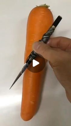 a hand holding a pen and pointing at an orange carrot