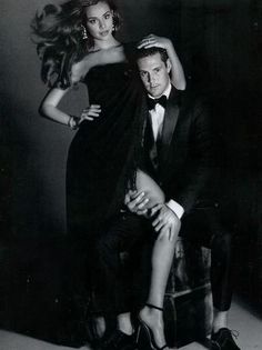 a man sitting next to a woman on top of a chair in a black dress