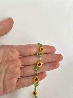 a hand holding a beaded bracelet with sunflowers and leaves on the end