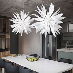 two white flowers hanging from the ceiling above a dining room table with fruit on it