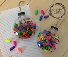 two glass ornaments with writing on them sitting on top of a piece of paper next to colored crayons